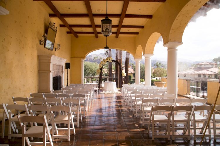 The image shows a beautifully decorated outdoor venue set up for a wedding ceremony, with rows of chairs facing an archway.