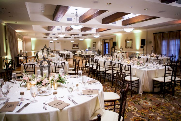 A decorated banquet hall with round tables and chairs arranged for an event, possibly a wedding reception or formal dinner, with elegant table settings.