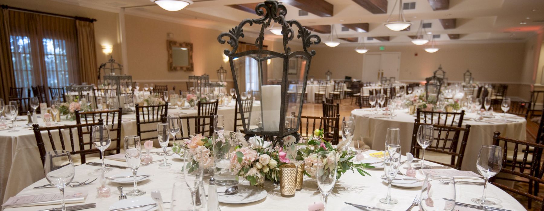 A decorated banquet hall with round tables set with fine china, glassware, floral centerpieces, and a large decorative candle holder.