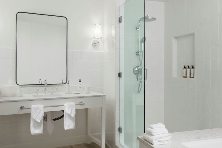 This image shows a modern bathroom with a large mirror, a sink with towels, a glass-enclosed shower, and a bathtub beside a small stack of towels.