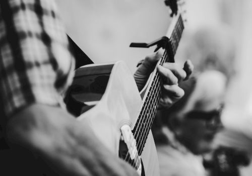 A person is playing an acoustic guitar, and another person is in the background holding a string instrument, possibly a violin.