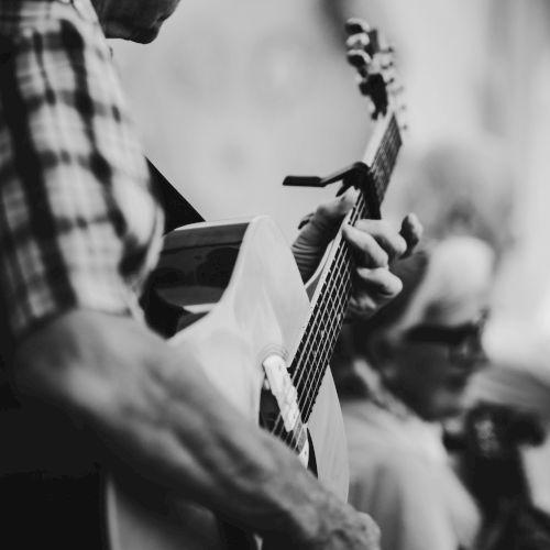 A person is playing an acoustic guitar, and another person is in the background holding a string instrument, possibly a violin.