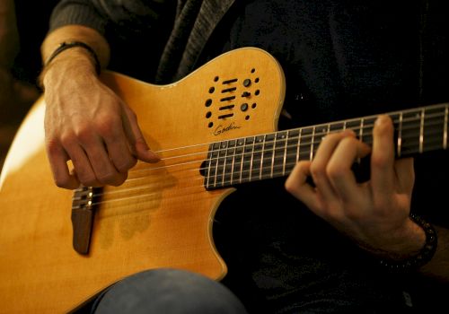 A person is playing a wooden acoustic guitar, strumming with one hand while forming chords with the other, wearing casual attire.