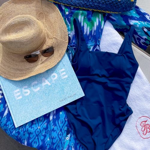 The image shows a sun hat, sunglasses, a blue swimsuit, a blue patterned cover-up, a towel, and a sign that says 