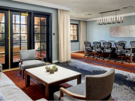 A modern office space features a sitting area with chairs and a table, adjacent to a conference room with a large table and office chairs.