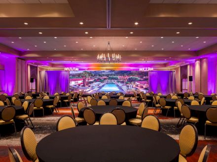 A large conference room with round tables and chairs, a colorful backdrop, and purple lighting creating a vibrant atmosphere, ending the sentence.